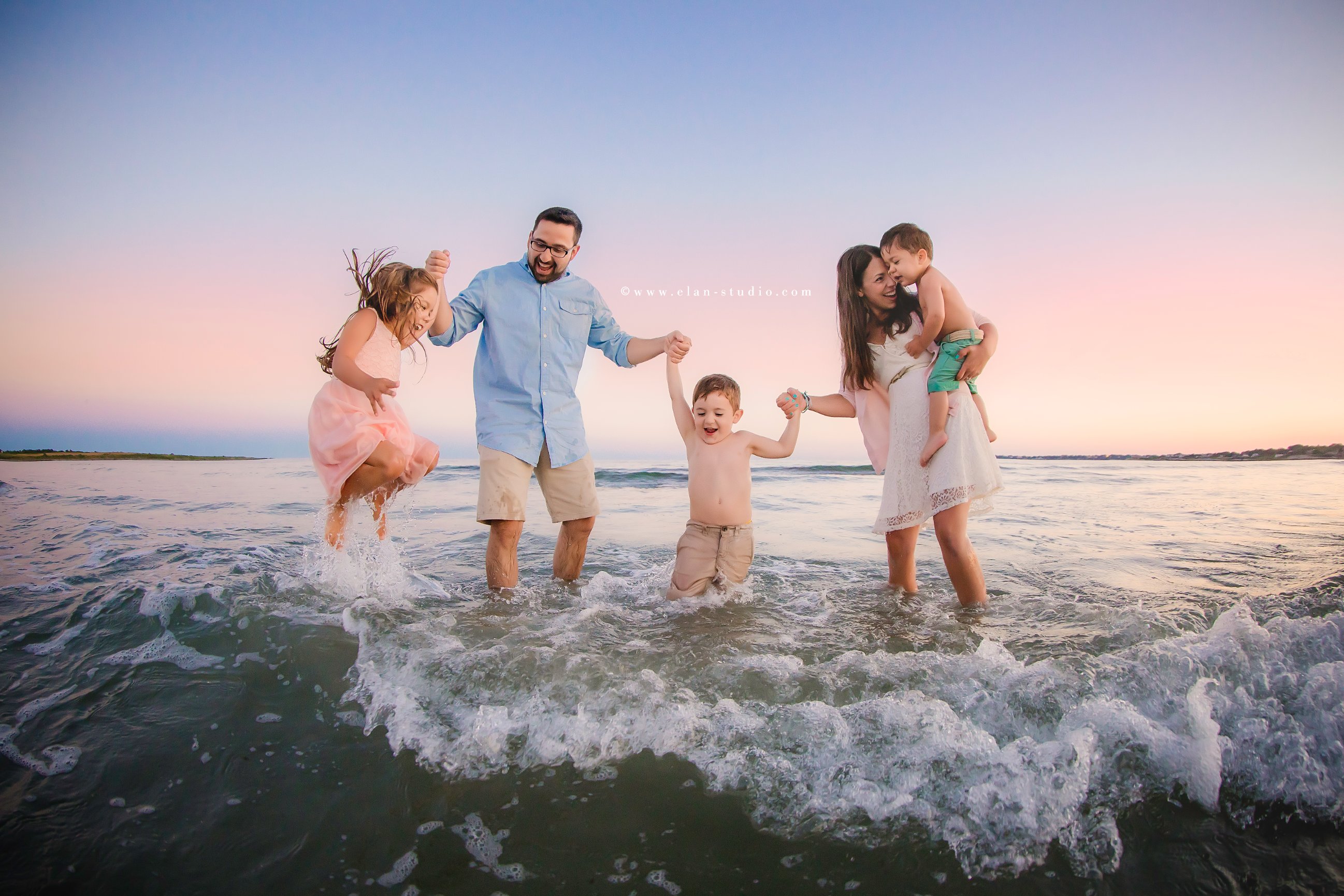 family jumping in the ocean waves at sunset