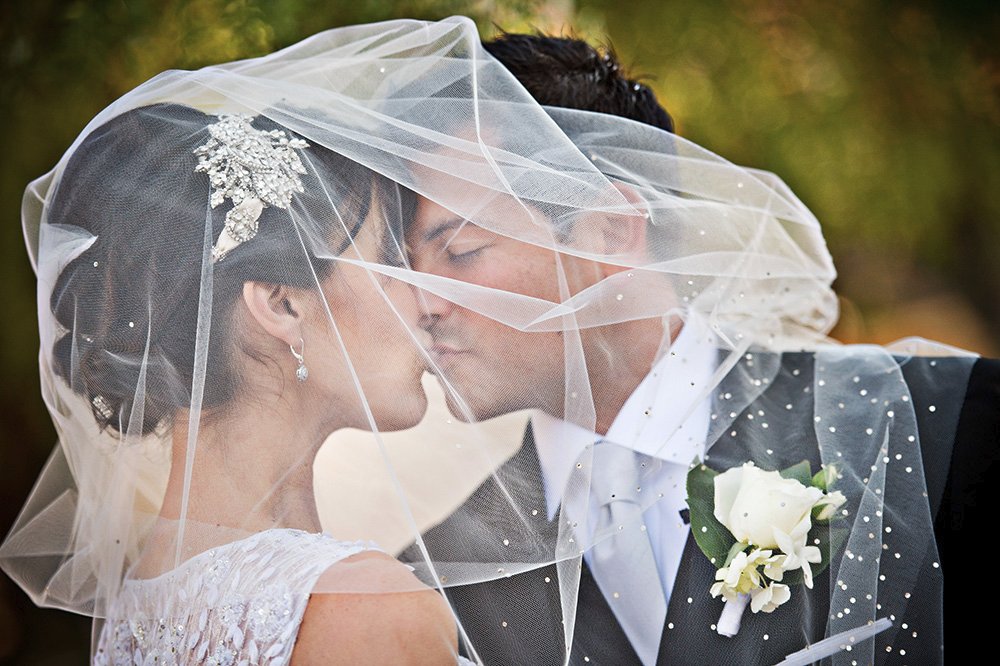 Bride and Groom kiss beneath jeweled wedding veil