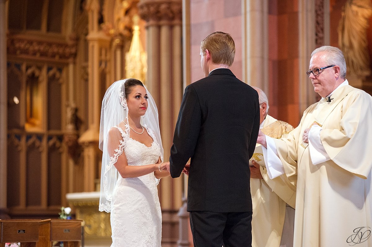 bride putting on groom's wedding band catholic church ceremony