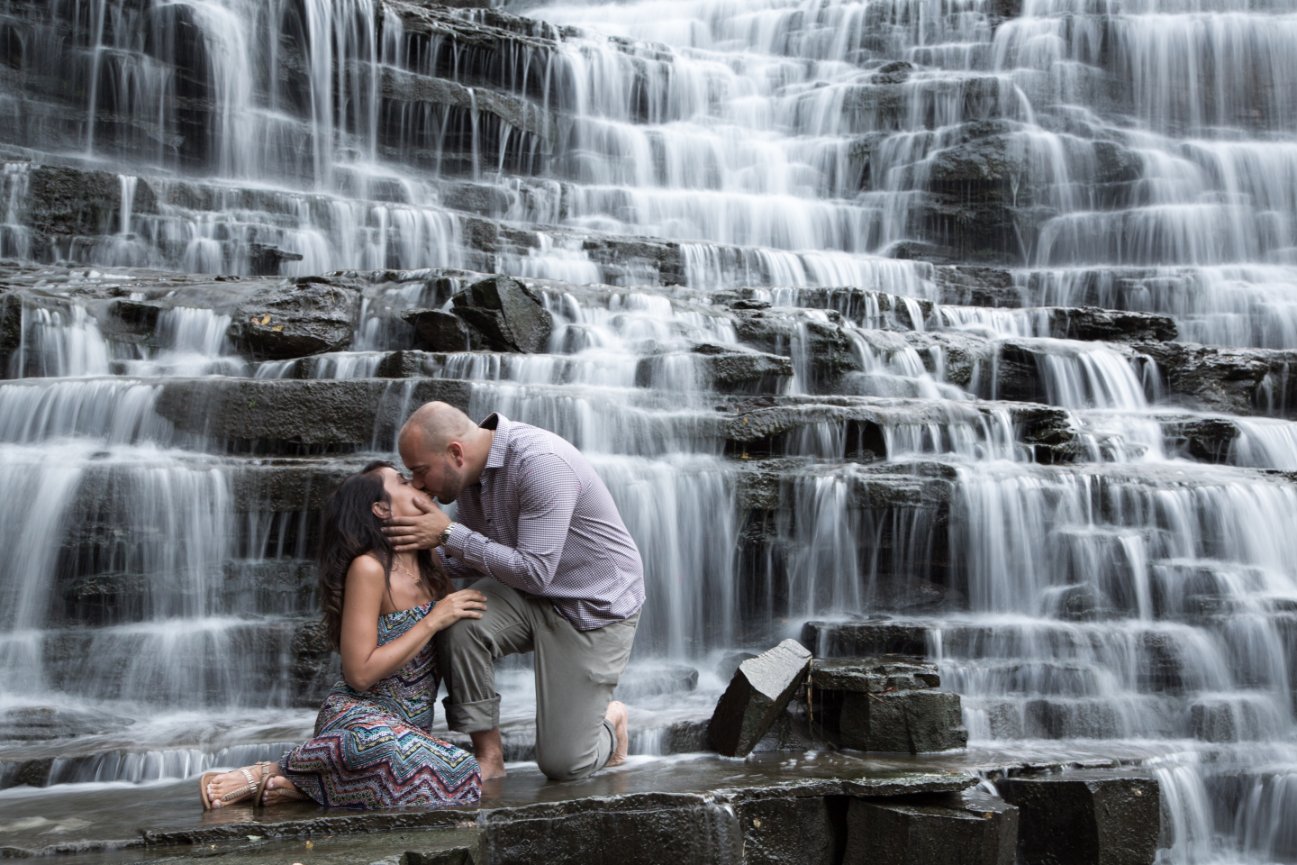A couple kisses in front of a tiered waterfall on a rocky ledge. Mount Albion Falls