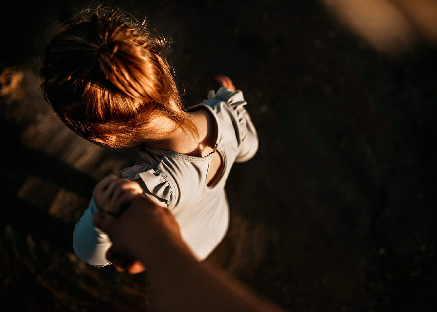 toddler girl holding a parent's hand, looking down at the top of a child's head