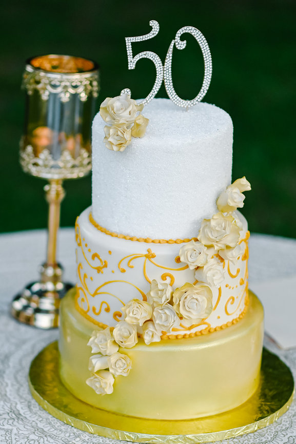 Three-tiered birthday cake adorned with yellow roses, gold accents, and a sparkling 50 topper, elegantly presented.