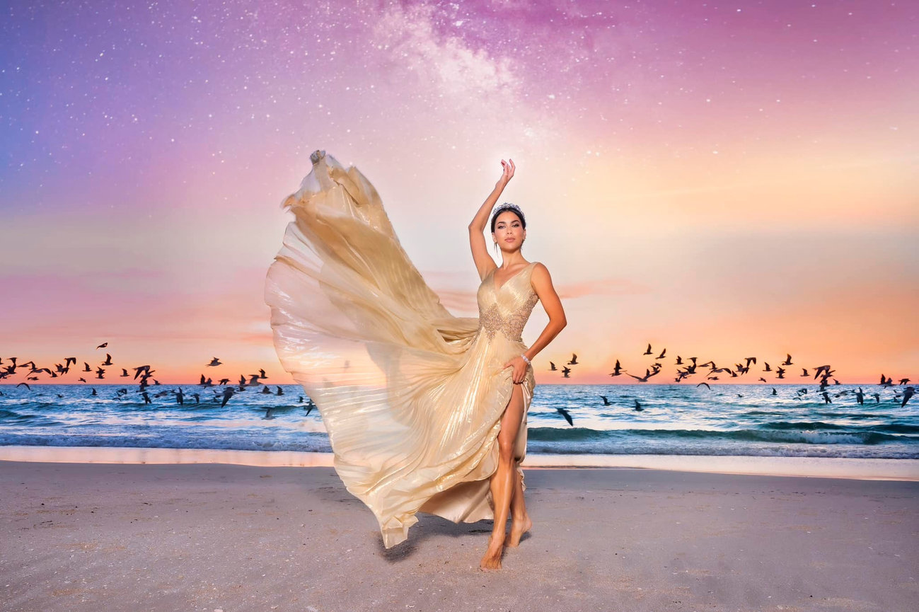 Woman in a flowing golden gown dances on the beach at sunset, with birds flying in the background.