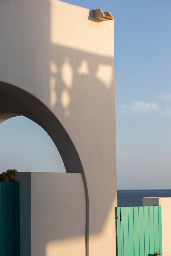 White arch and turquoise gate with ocean view under a clear blue sky.