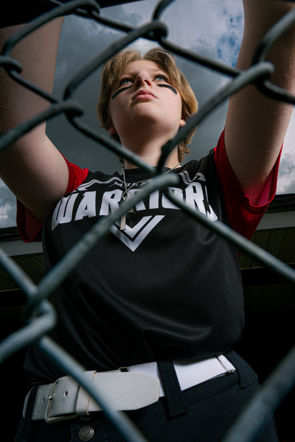 softball player leaning against the fence watching the game
