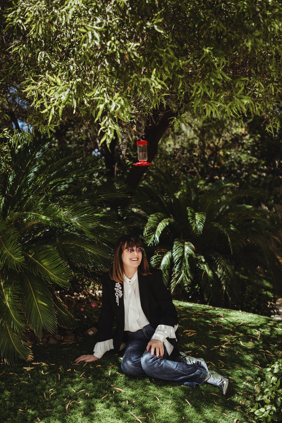 Barbara Molasky portrait outdoors in lovely garden scape in denim with velevet coat and white blouse, portrait picture taken by Adam Trujillo, a Las Vegas portrait photographer.