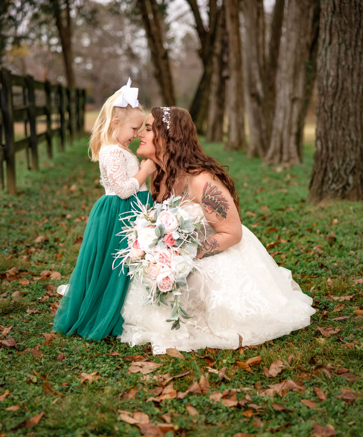 Bride kneeling in her lace gown, touching noses with her flower girl in a green dress during a heartfelt countryside wedding captured by Fairhope, alabama photographer Dixon Creative Images