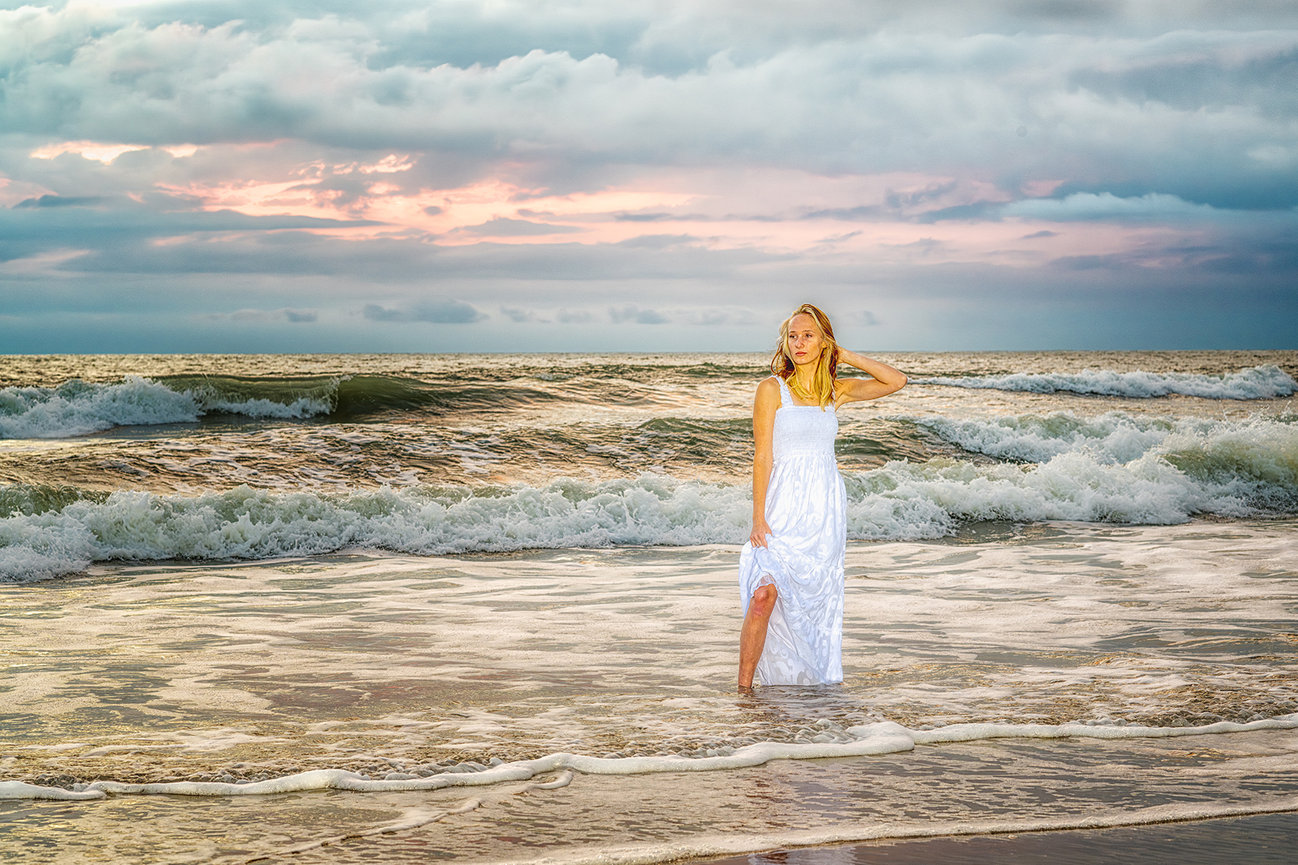 Senior in white maxi dress walking through ocean surf at cinematic sunset, fine art coastal masterpiece, Galveston frame, by Swartz Portraits Texas