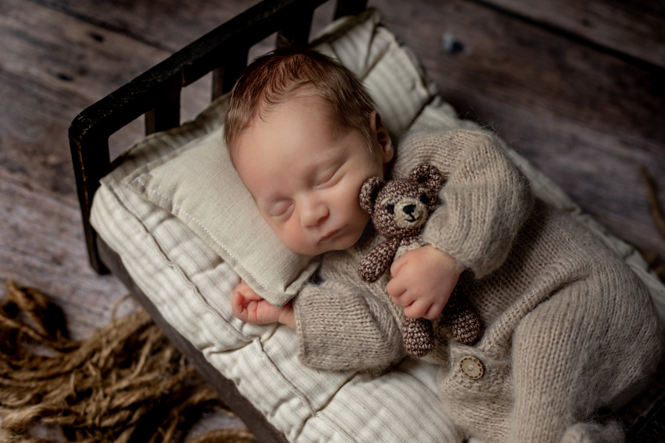 Newborn baby tucked in bed with a teddy bear