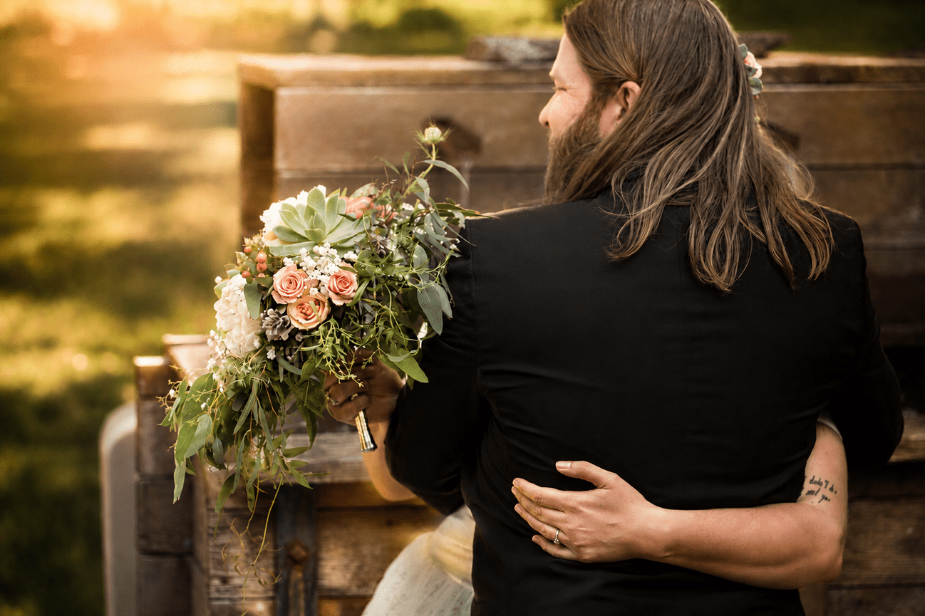 Woman embracing a partner on a bench beside a bouquet of flowers in golden light.