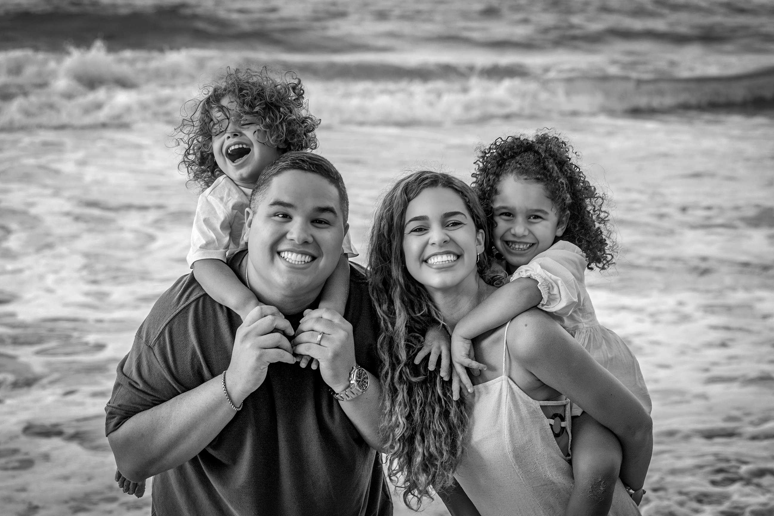 Black-and-white family portrait of parents embracing their children by the sea, by Rafael Sotomayor