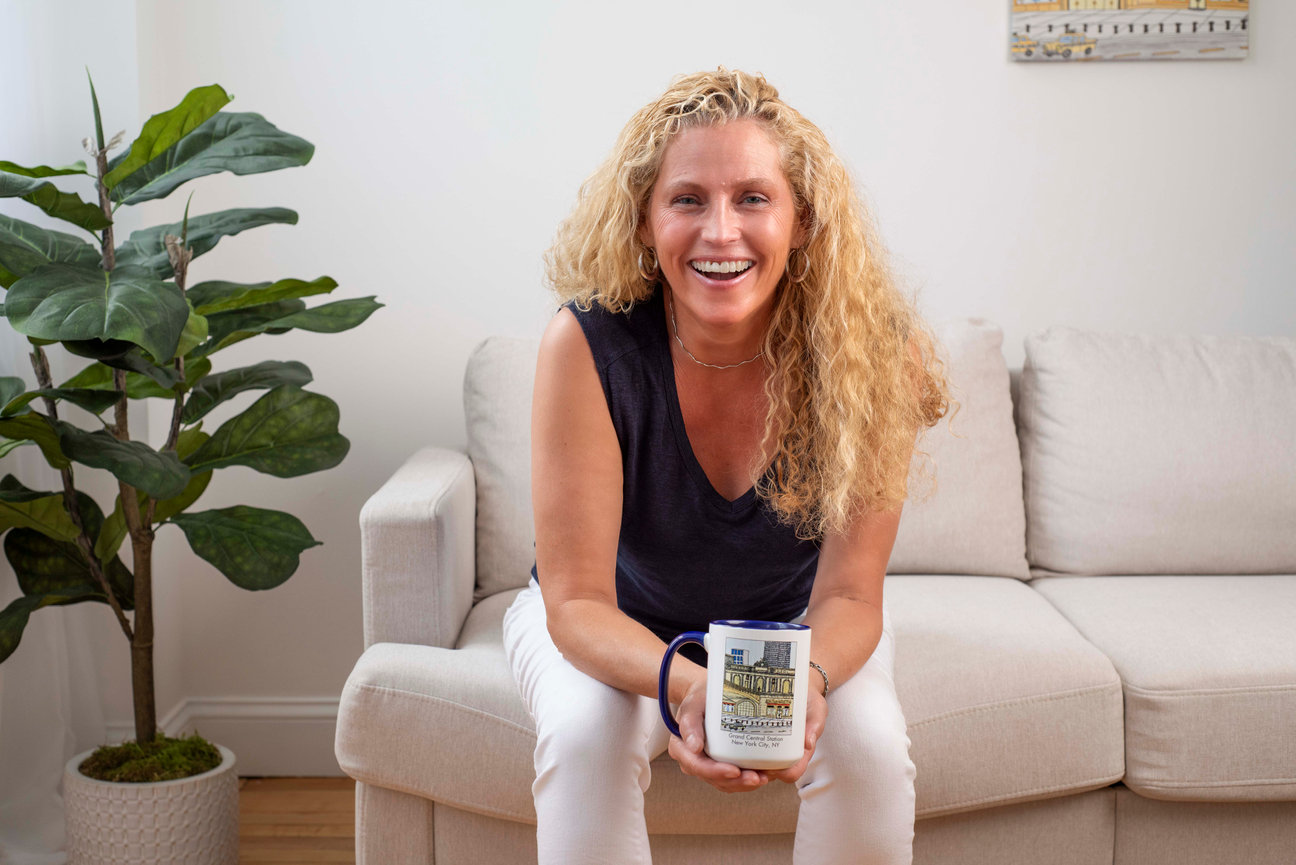 Woman sitting on couch smiling drinking from a mug