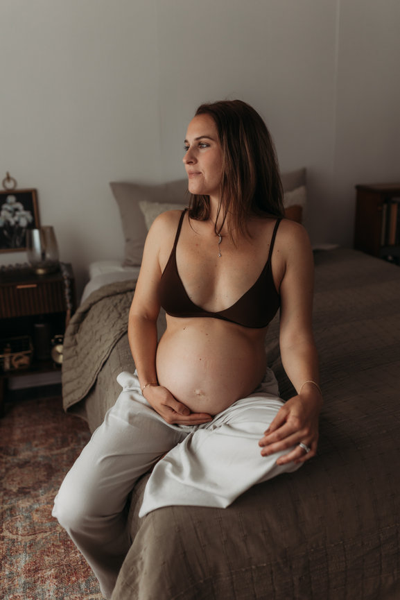 A pregnant woman sitting on a bed during her New Jersey Maternity Photography session.