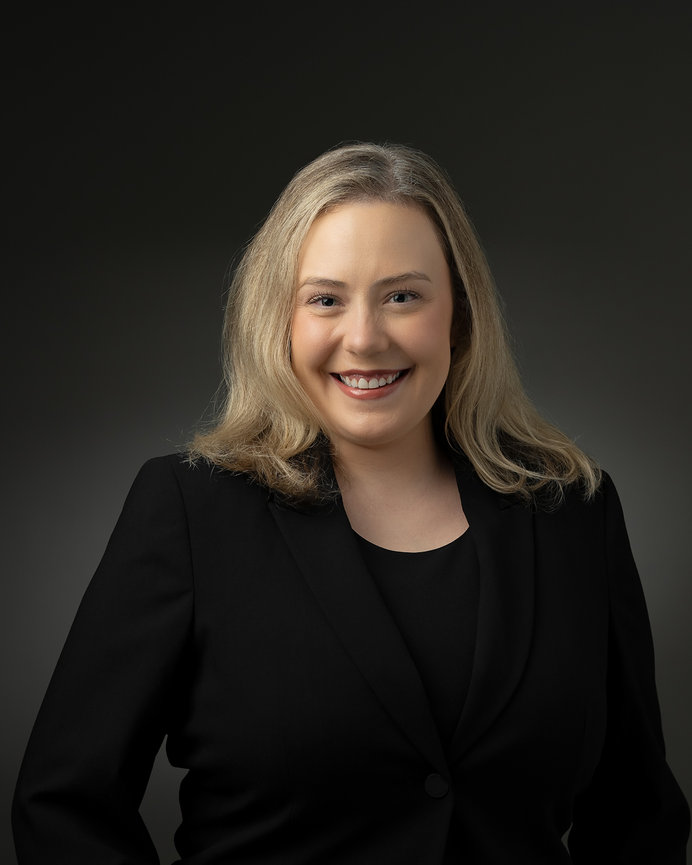 Smiling person wearing a black suit against a dark background.