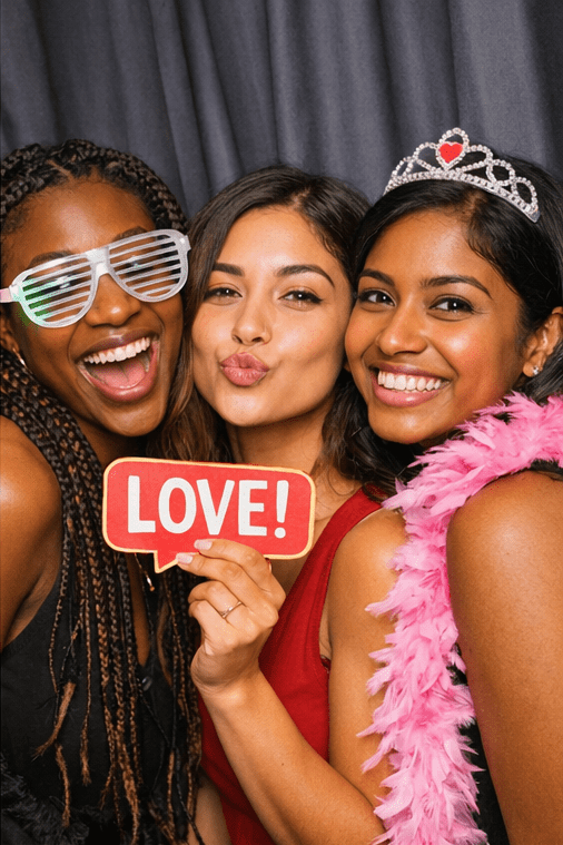 Three women smiling with party props in a photo booth