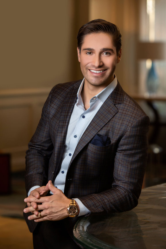 Smiling man in a plaid blazer and dress shirt posing indoors by a table