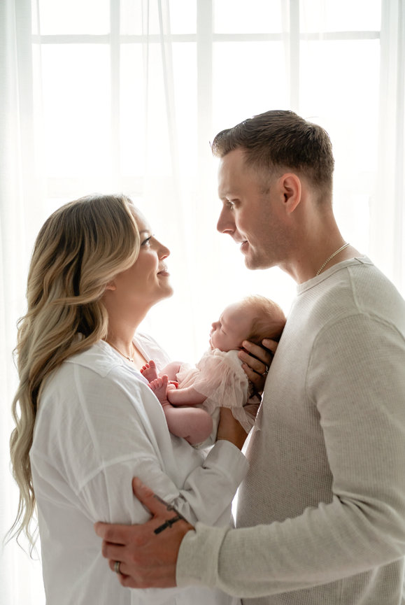 New parents holding their newborn baby in a bright window-lit room- Studio San Diego Hillcrest