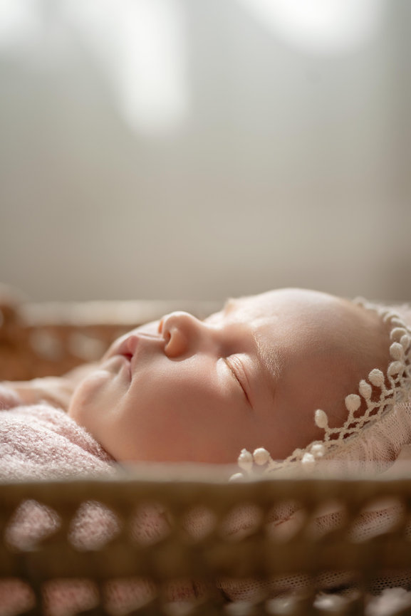 Sleeping newborn baby in a basket, wrapped in a soft pink blanket and lace bonnet