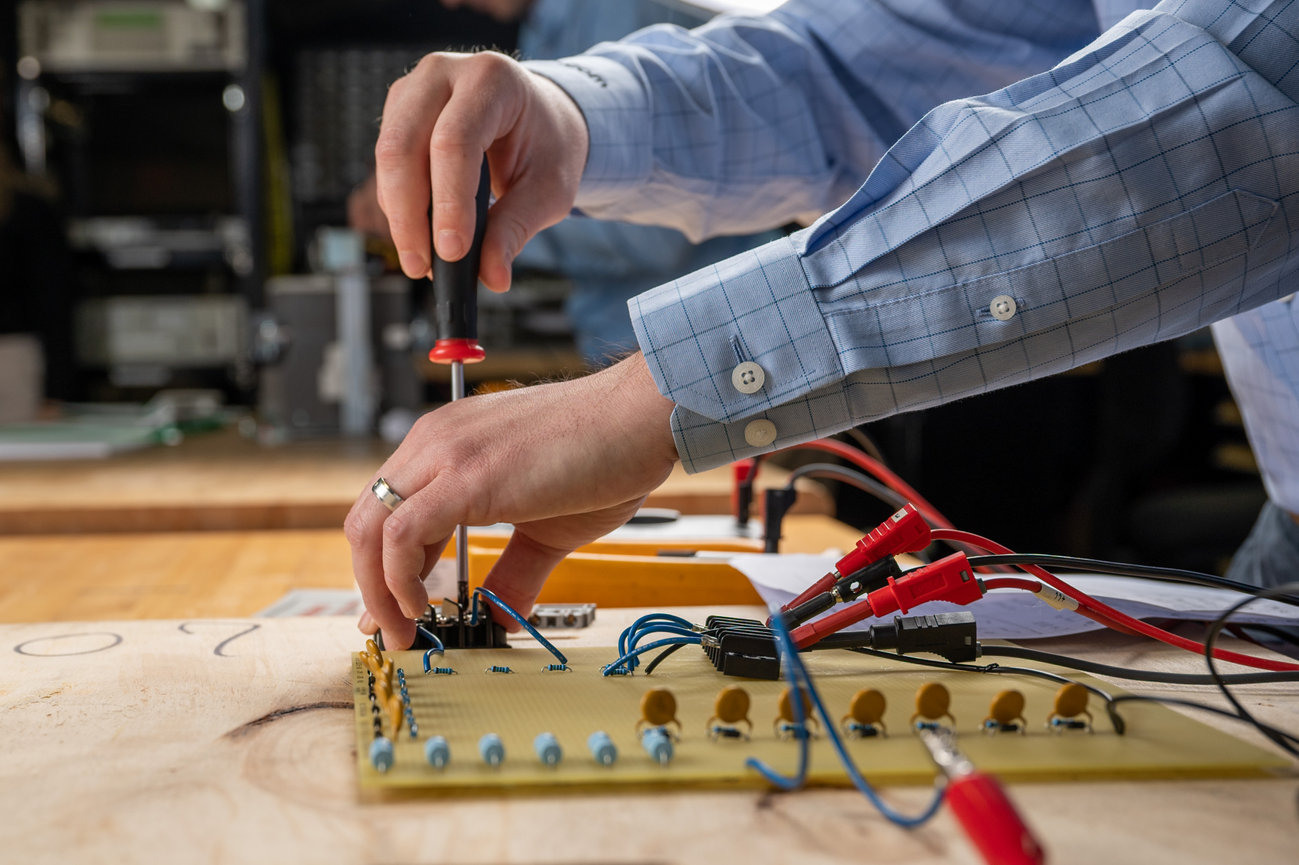 Person using a screwdriver to assemble an electronics circuit board with wires on a workbench