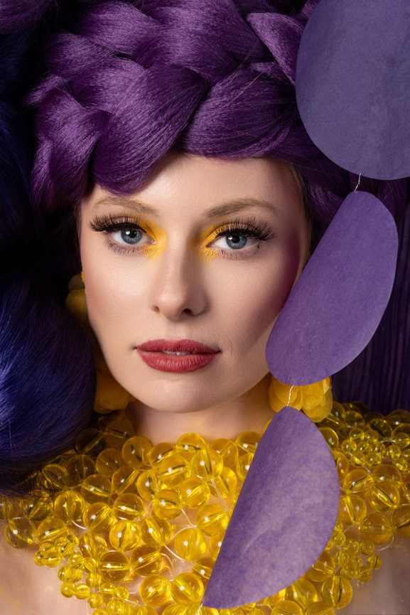 Close-up portrait of a model in Salt Lake City, Utah, featuring vibrant purple hair styled in intricate braids and bold yellow eye makeup. Captured by Tre Nelson Photo, showcasing creative beauty and avant-garde fashion.