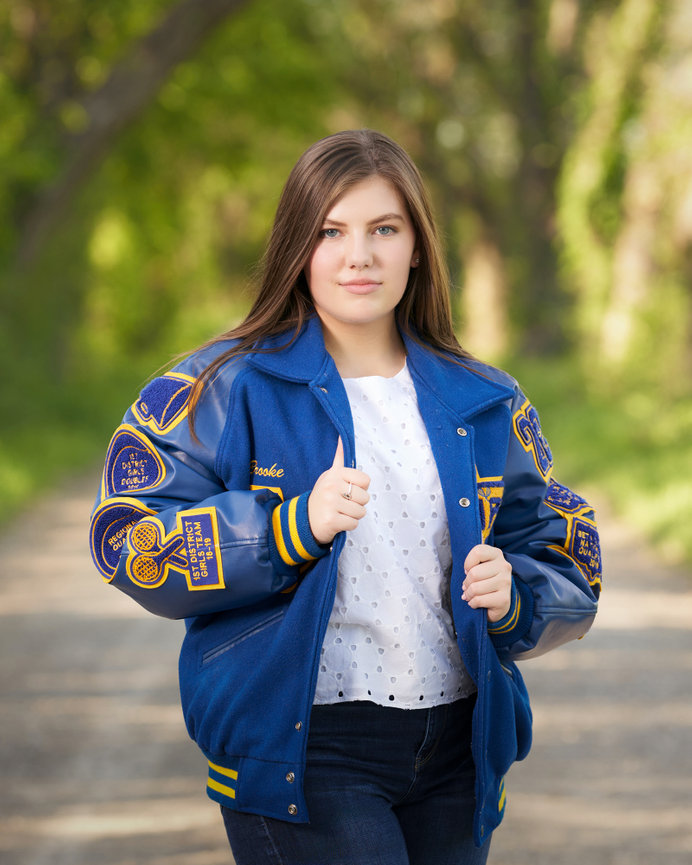 High school senior girl wearing letterman jacket portrait outdoors in Sherman TX highlighting school pride and achievements