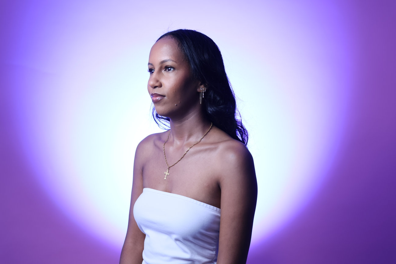 Portrait of a woman in a white top lit by purple studio light.