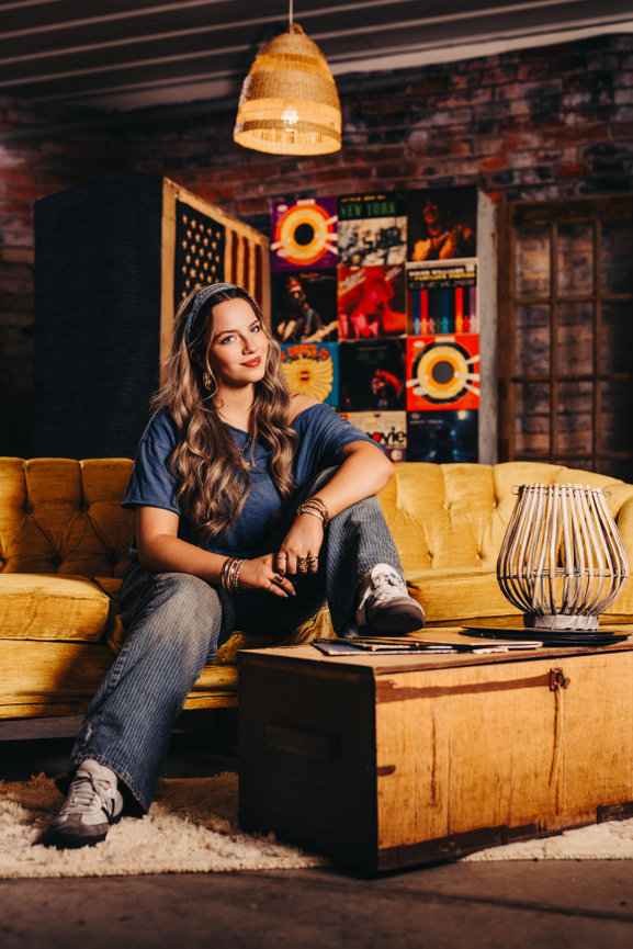 Woman sitting on a couch in a warm rustic room with colorful decor.