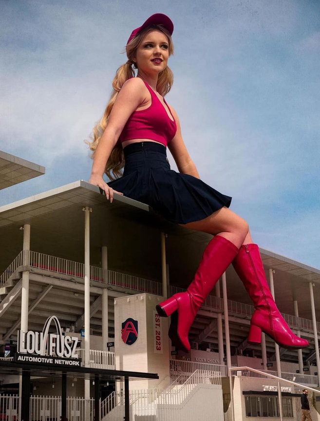 Woman in pink top and boots sitting atop large building with modern architecture.