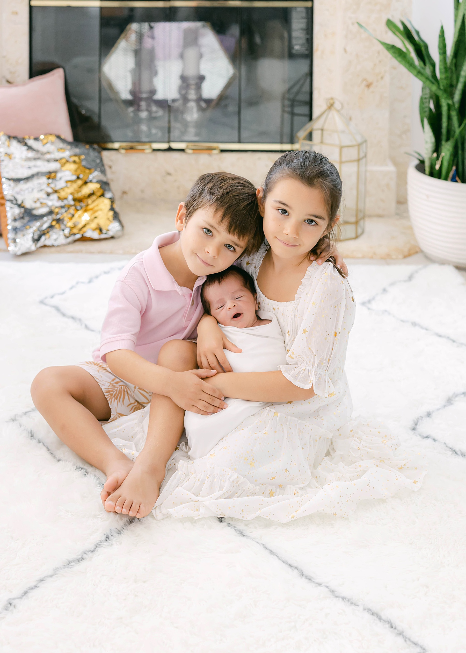 children holding newborn baby sitting on carpet in white clothing