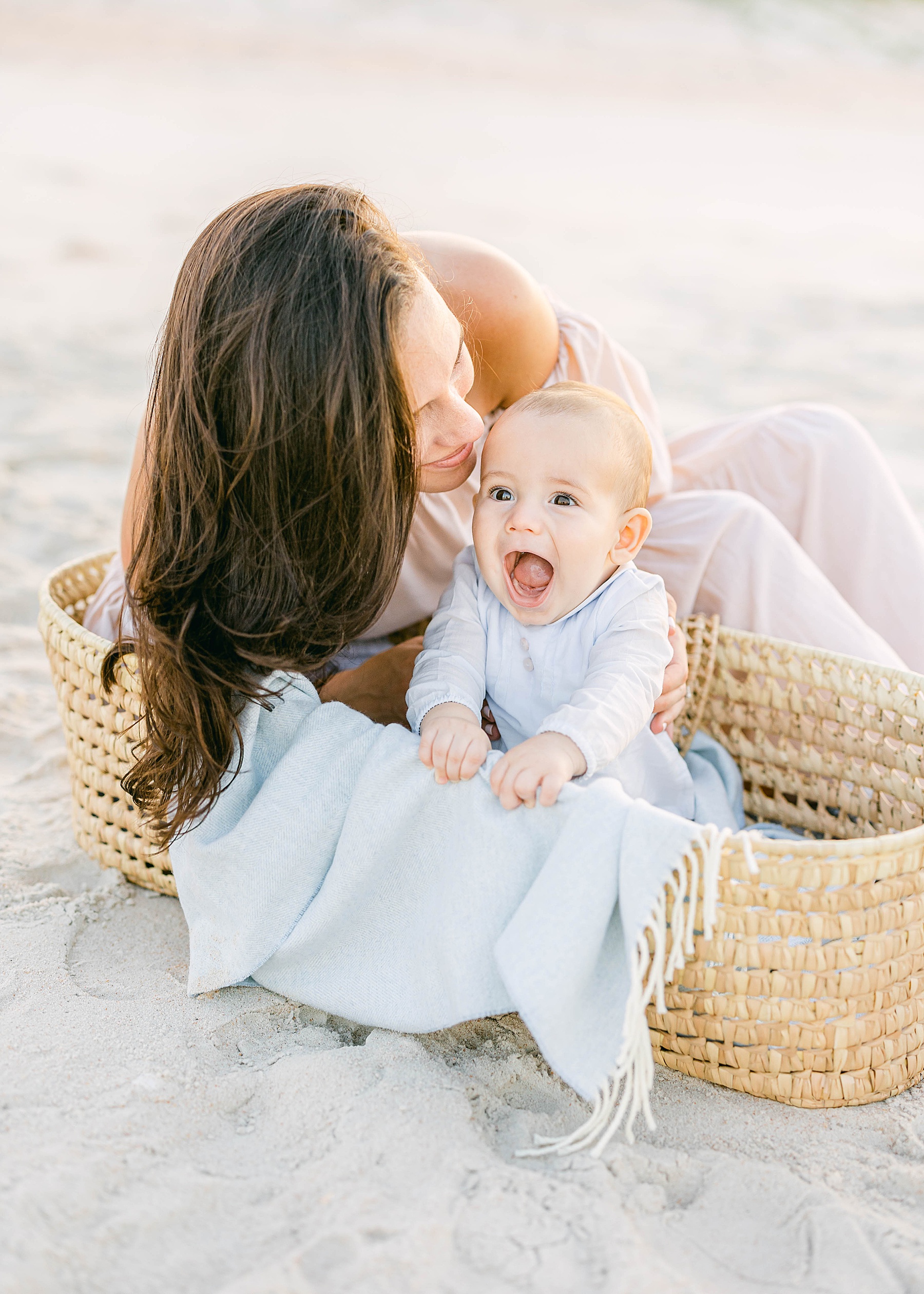 woman at the beach with baby boy sitting on the sand 