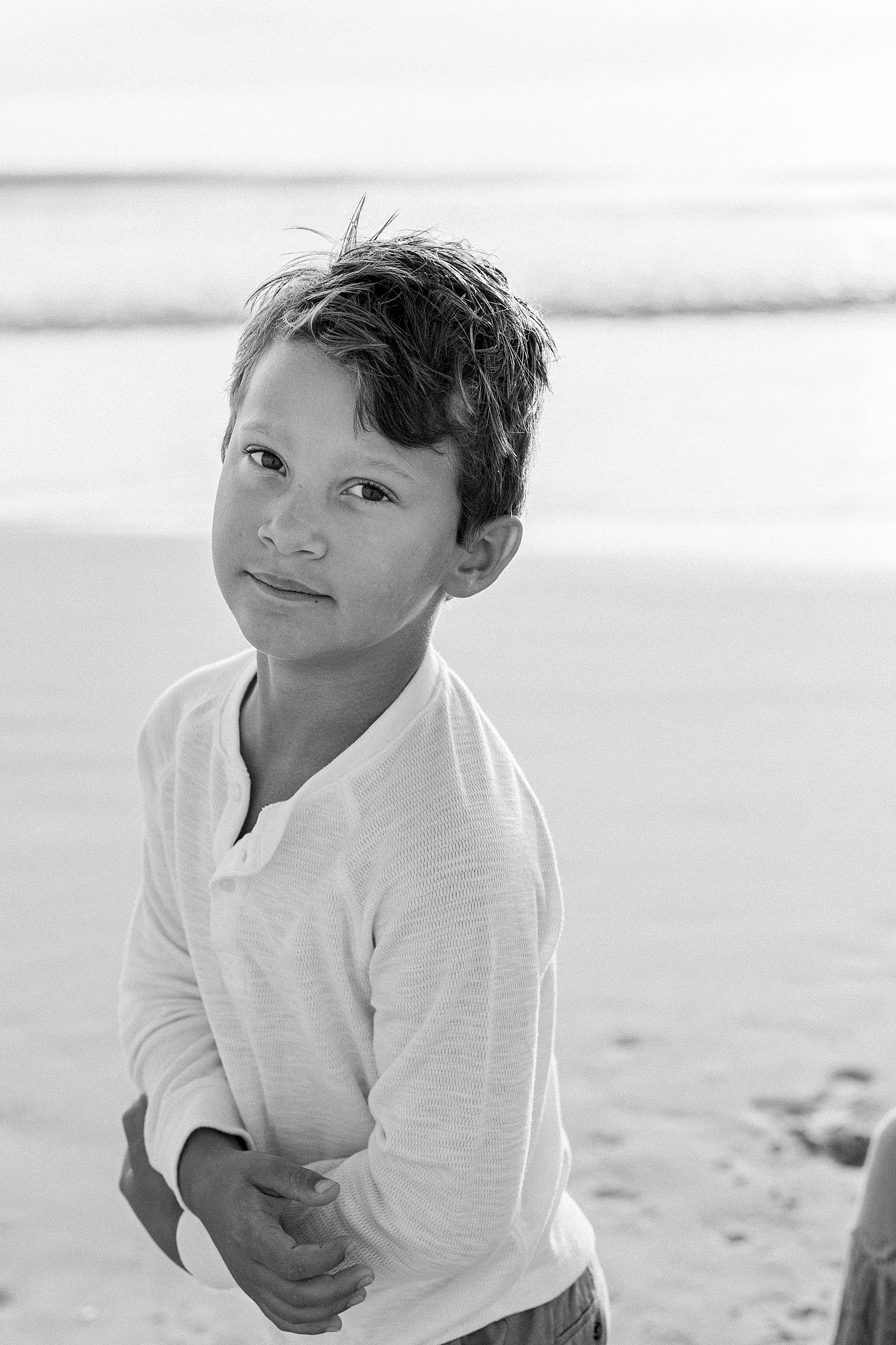 little boy in black and white on the beach looking at camera