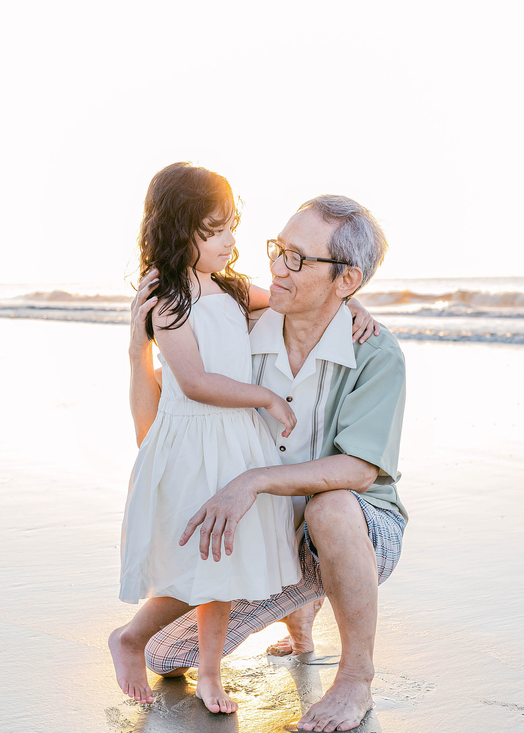old man holding little girl on the beach at sunrise