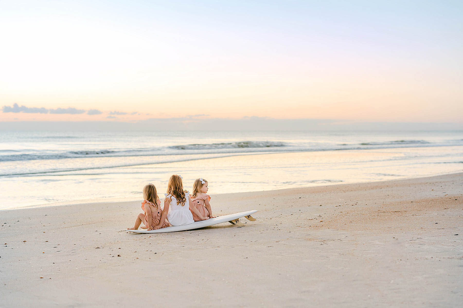 sunrise in ponte vedra beach with three little girls sitting on a white surfboard