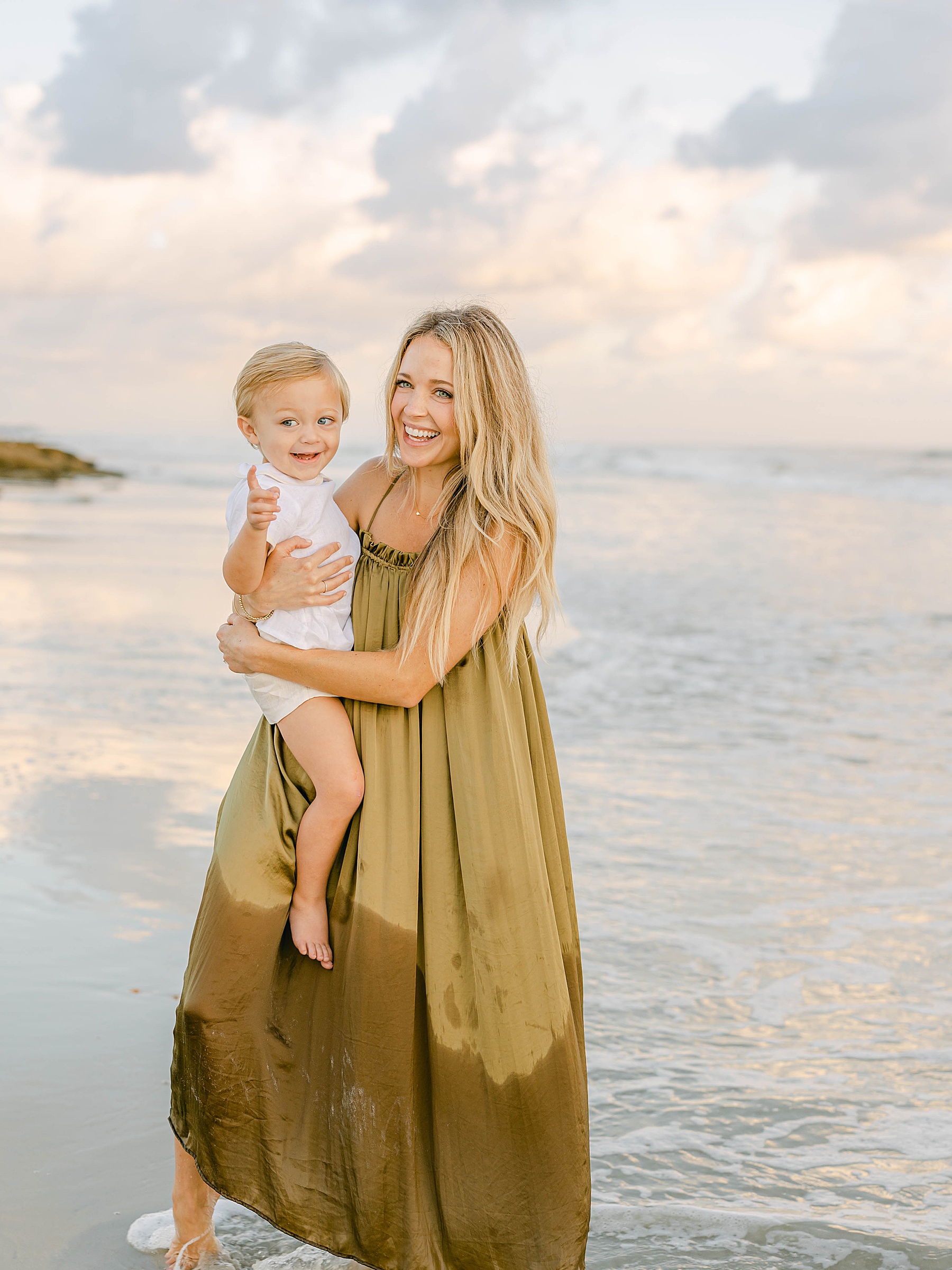 woman in green long dress holding baby boy on the beach