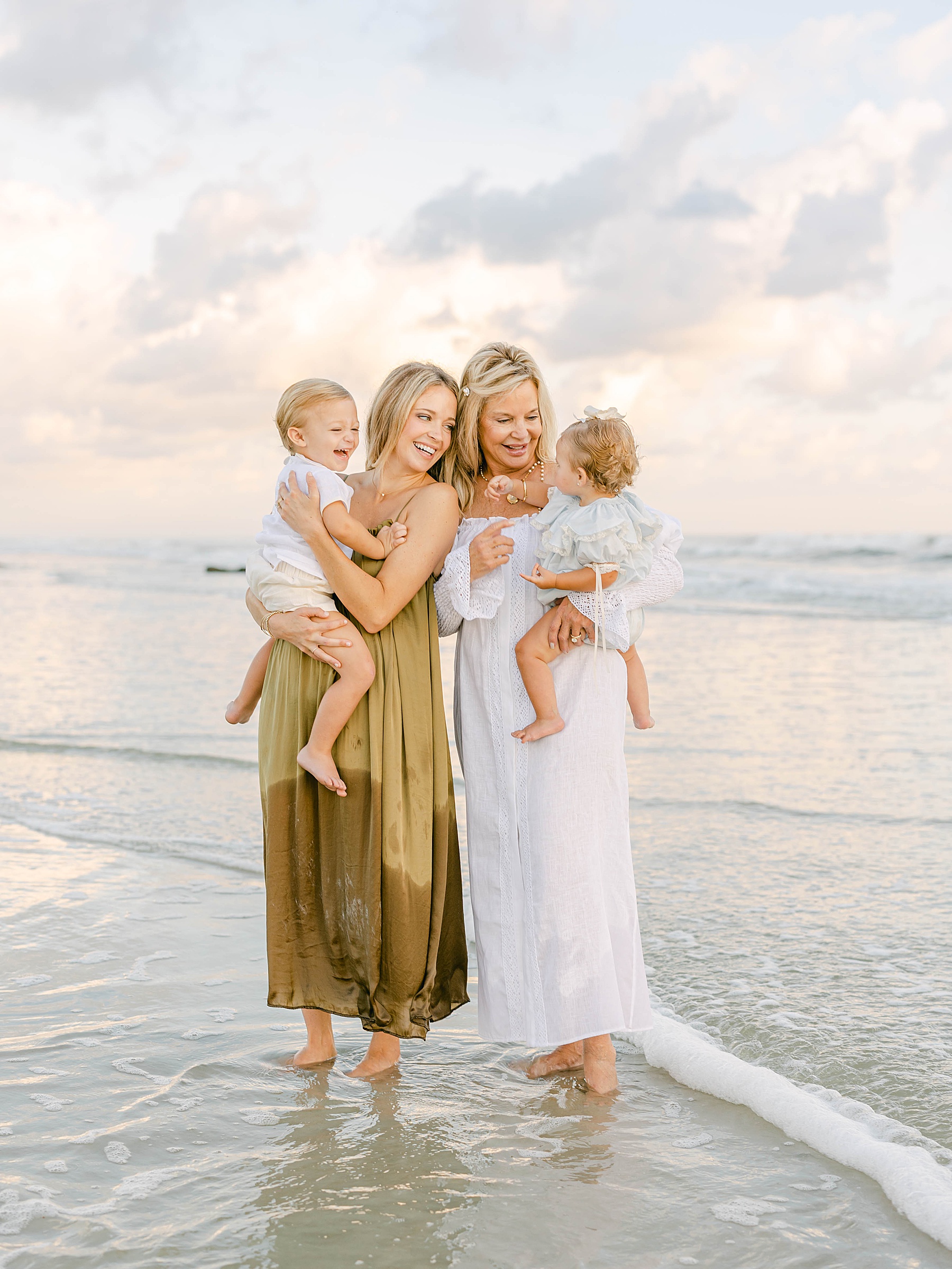 woman walking in the water at the beach at sunrise with children wearing neutral colors