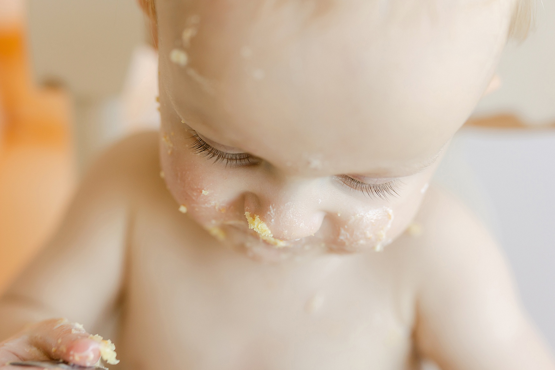baby boy looking down while eating yellow cake in white high chair with long eyelashes