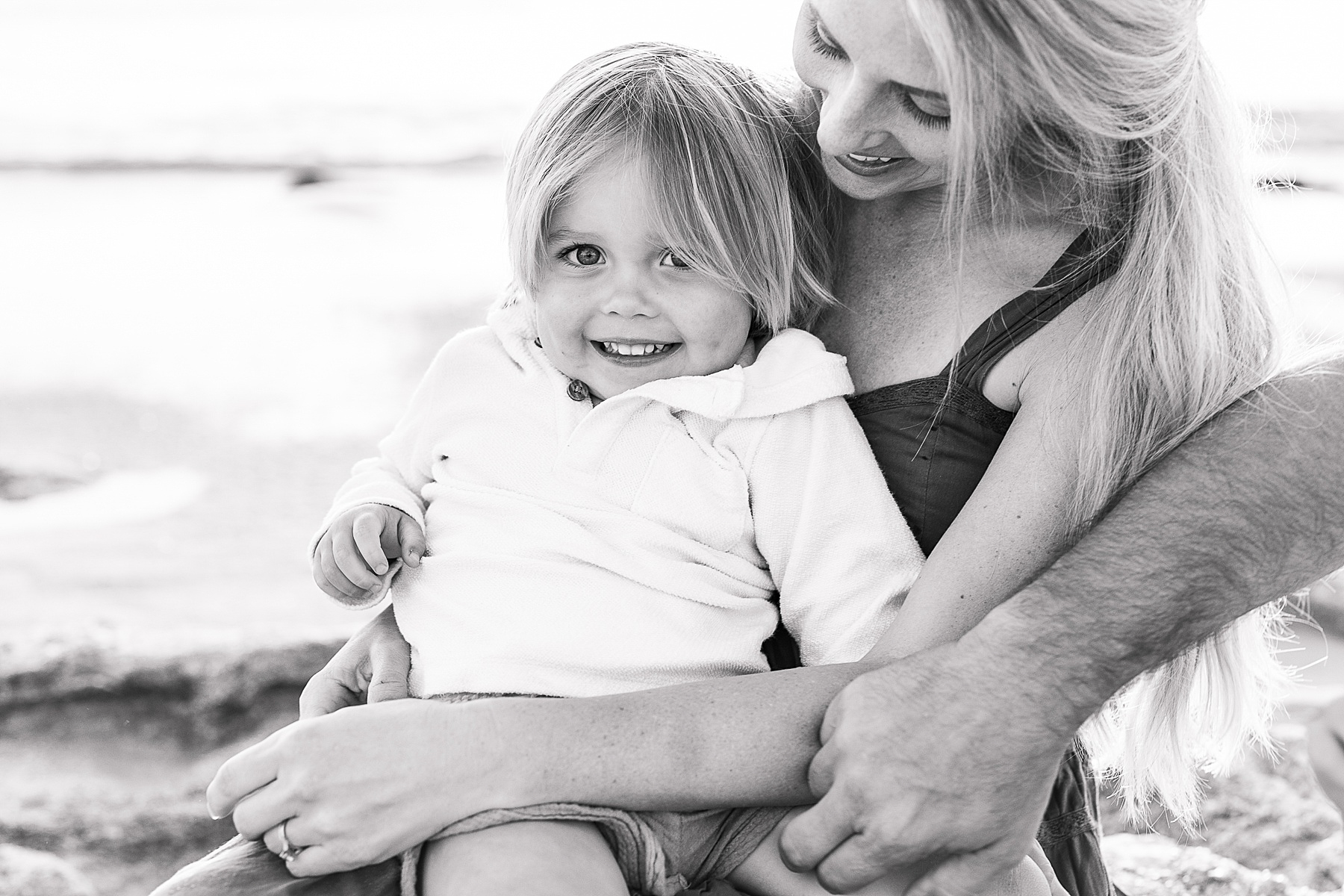 black and white family portrait of a woman holding a little boy on the beach at sunrise