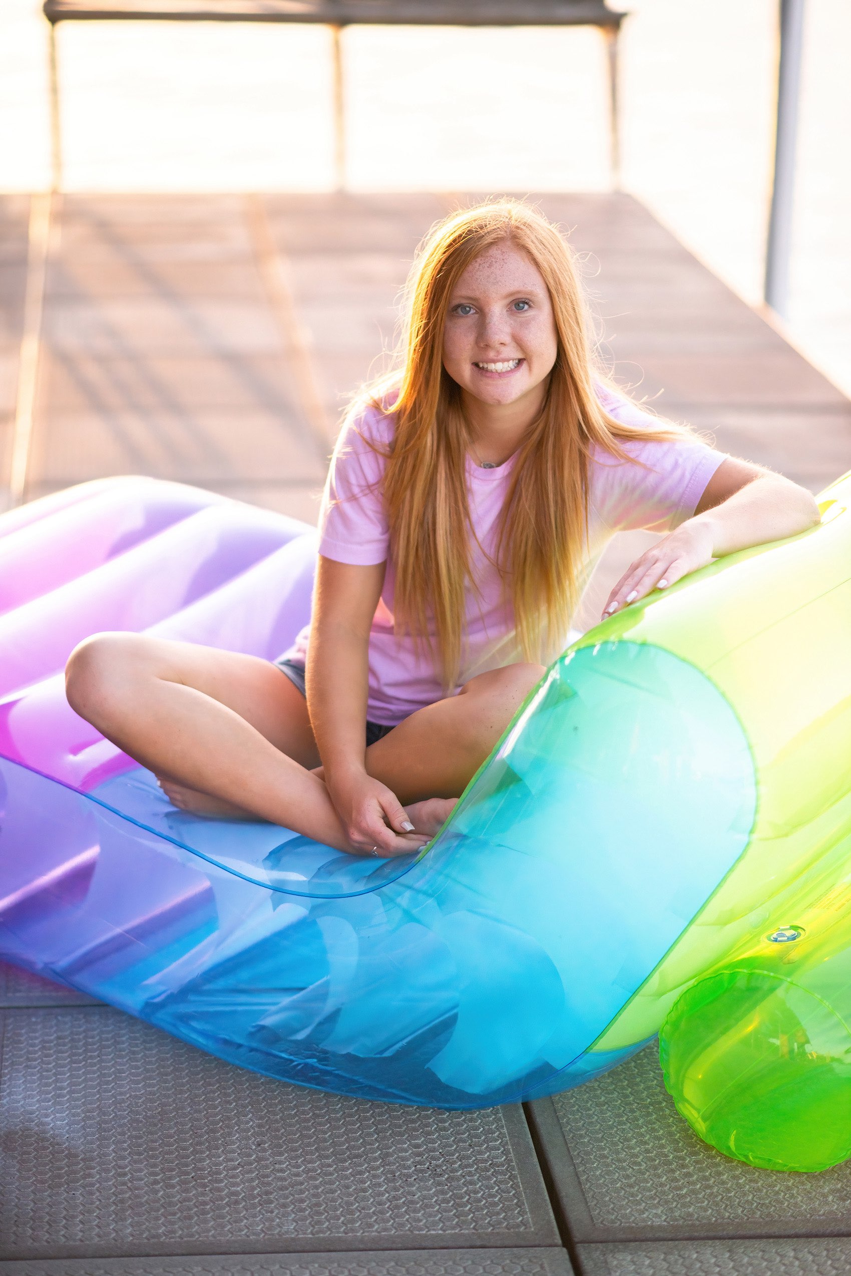 Senior girl in pink tshirt sitting on rainbow colored lounge chair.