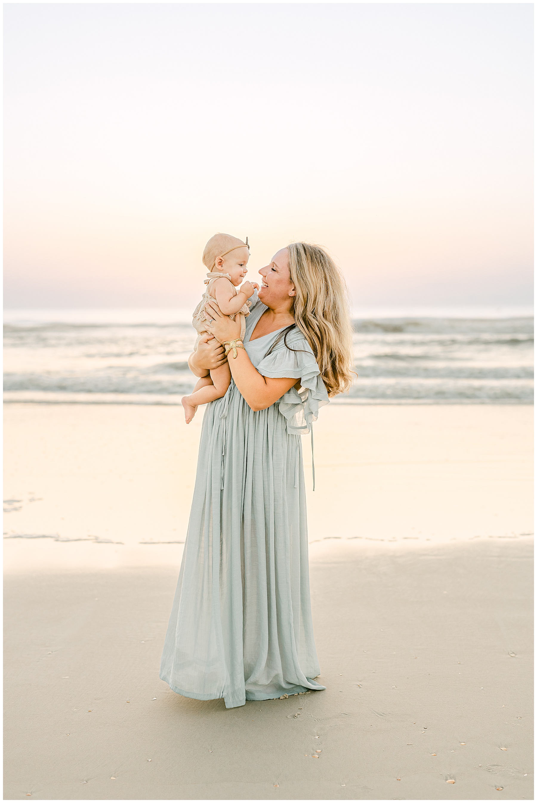 woman wearing green long dress holding baby girl at sunrise on the coast
