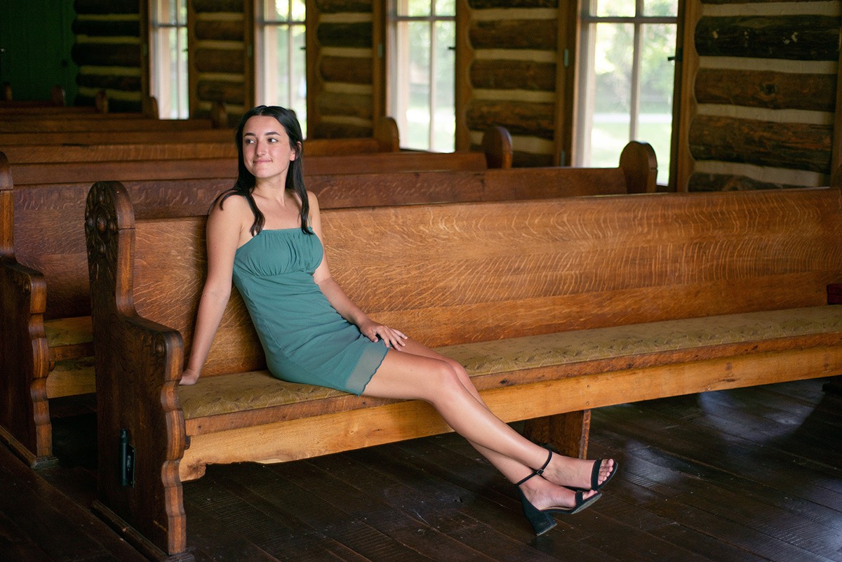 Senior girl in green dress sitting on church pew inside Hope Wilderness Chapel.