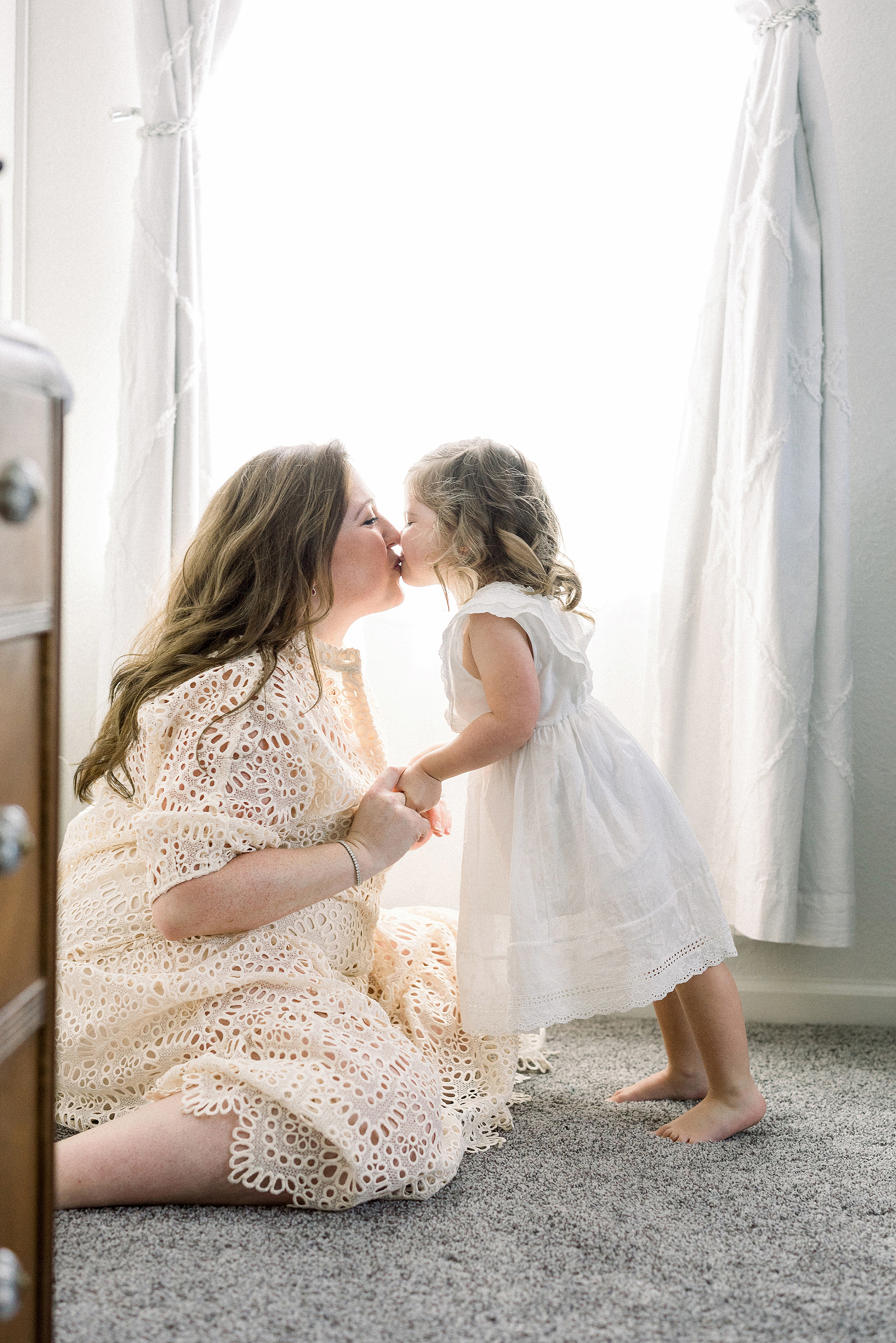 little girl kissing her mom near light and airy window with white sheers