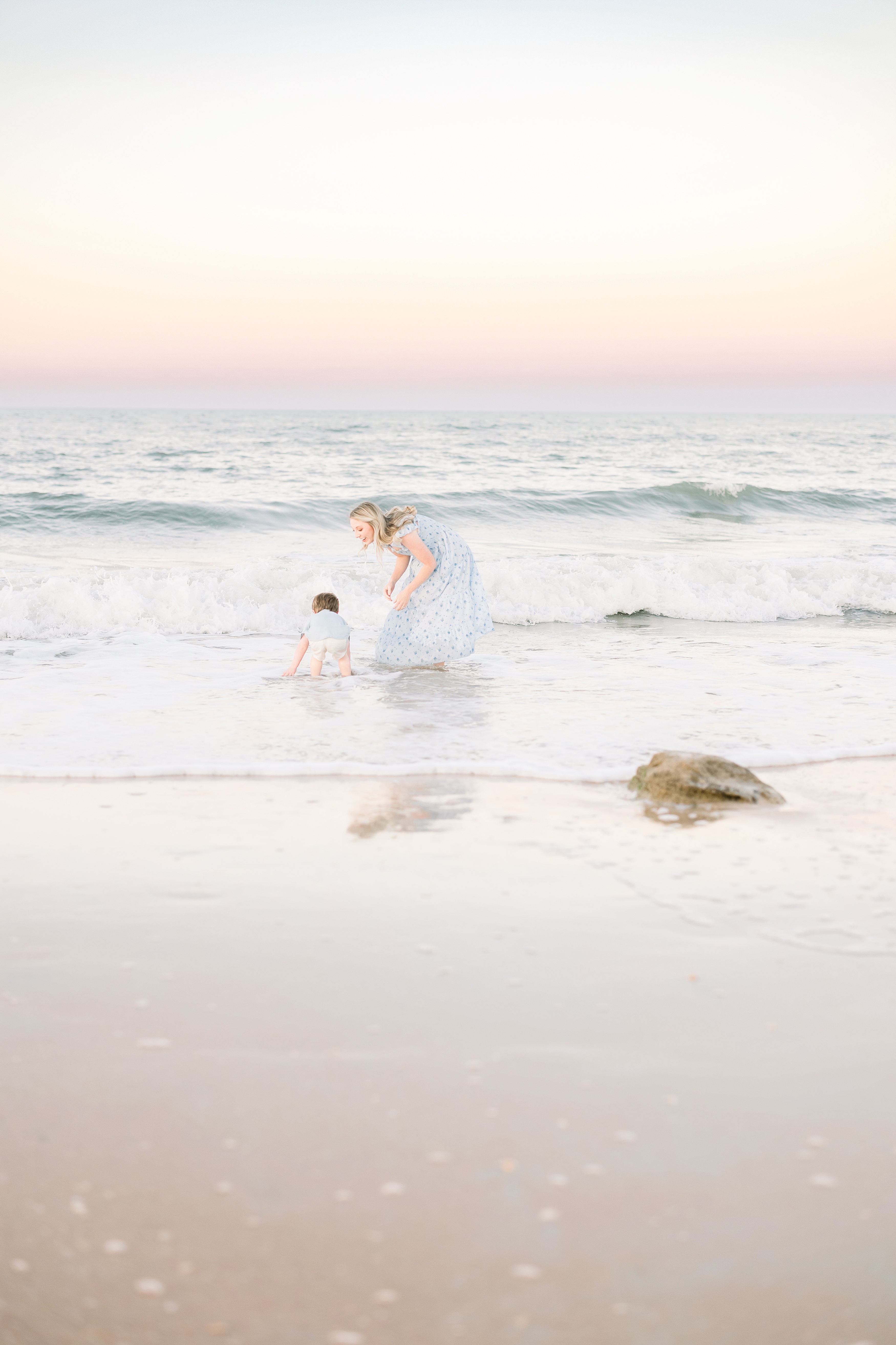 pastel portrait of woman in blue and white dress playing with little boy in the surf