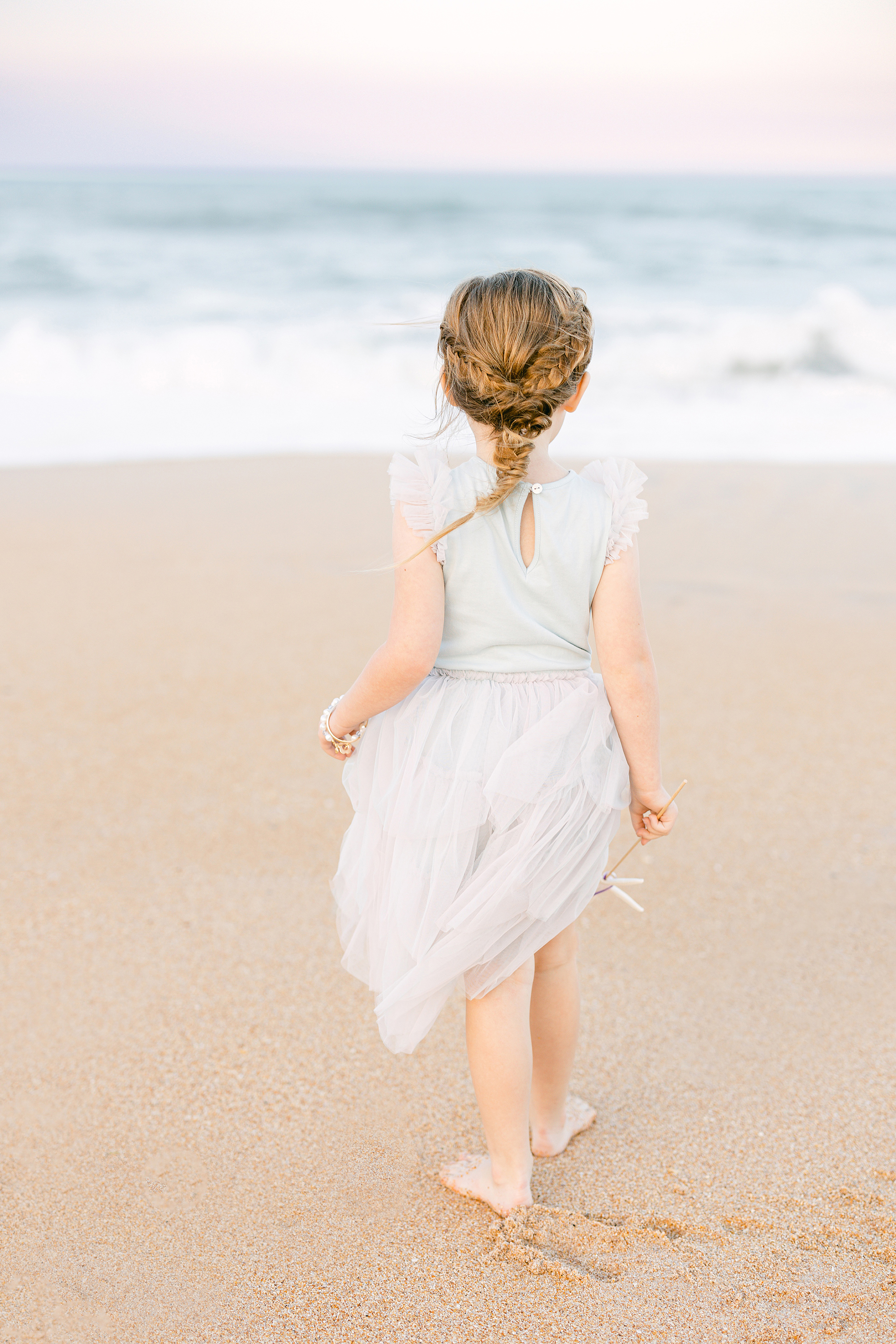 little girl with a mermaid braid in a pastel tutu dress standing near the ocean at sunset