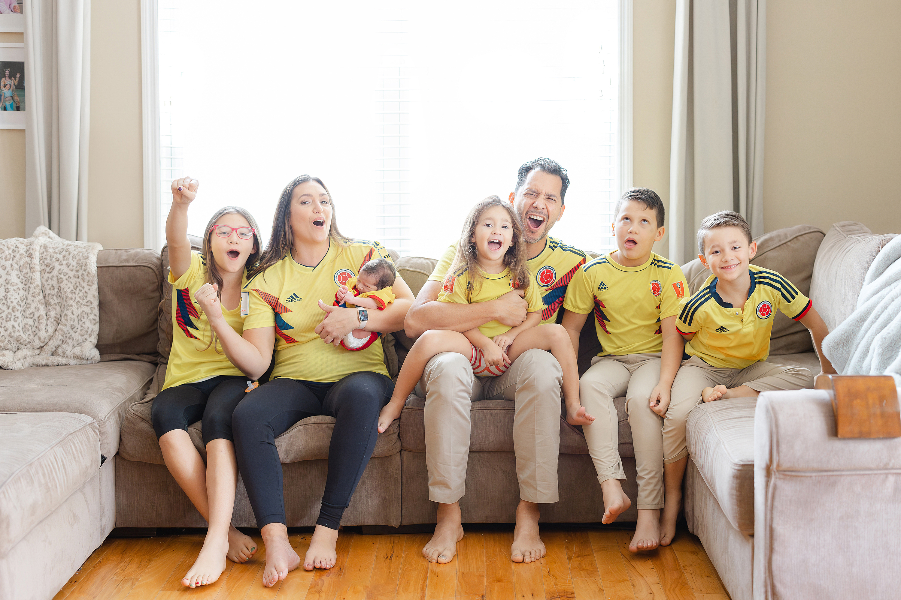 Family sitting on couch dressed in matching Colombia soccer jerseys.