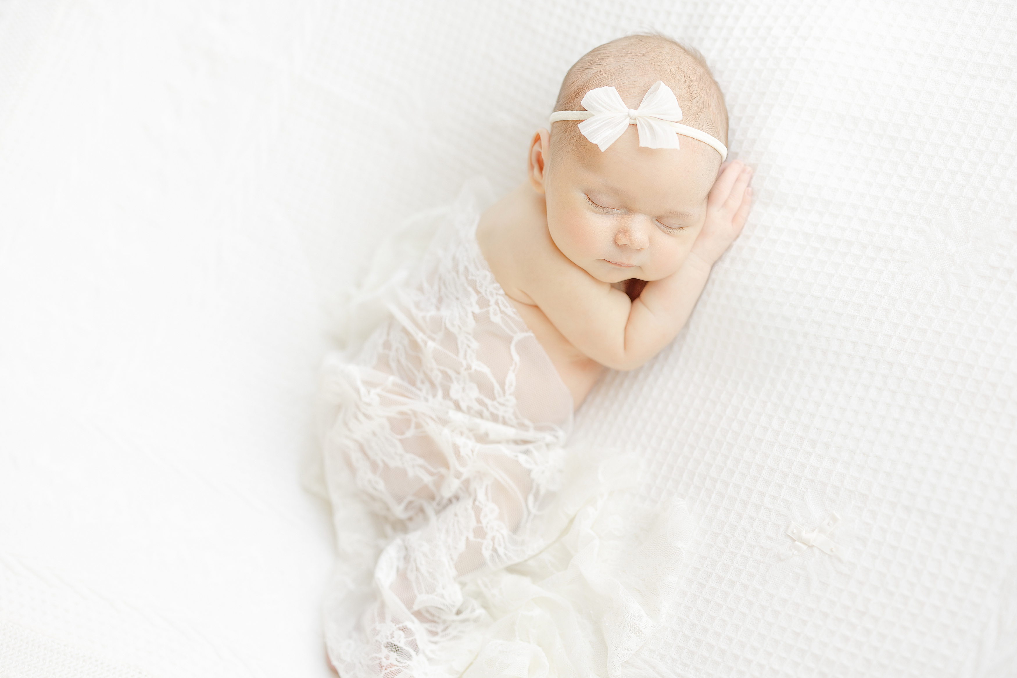 A light and airy newborn portrait of a baby girl in lace and cream blankets.