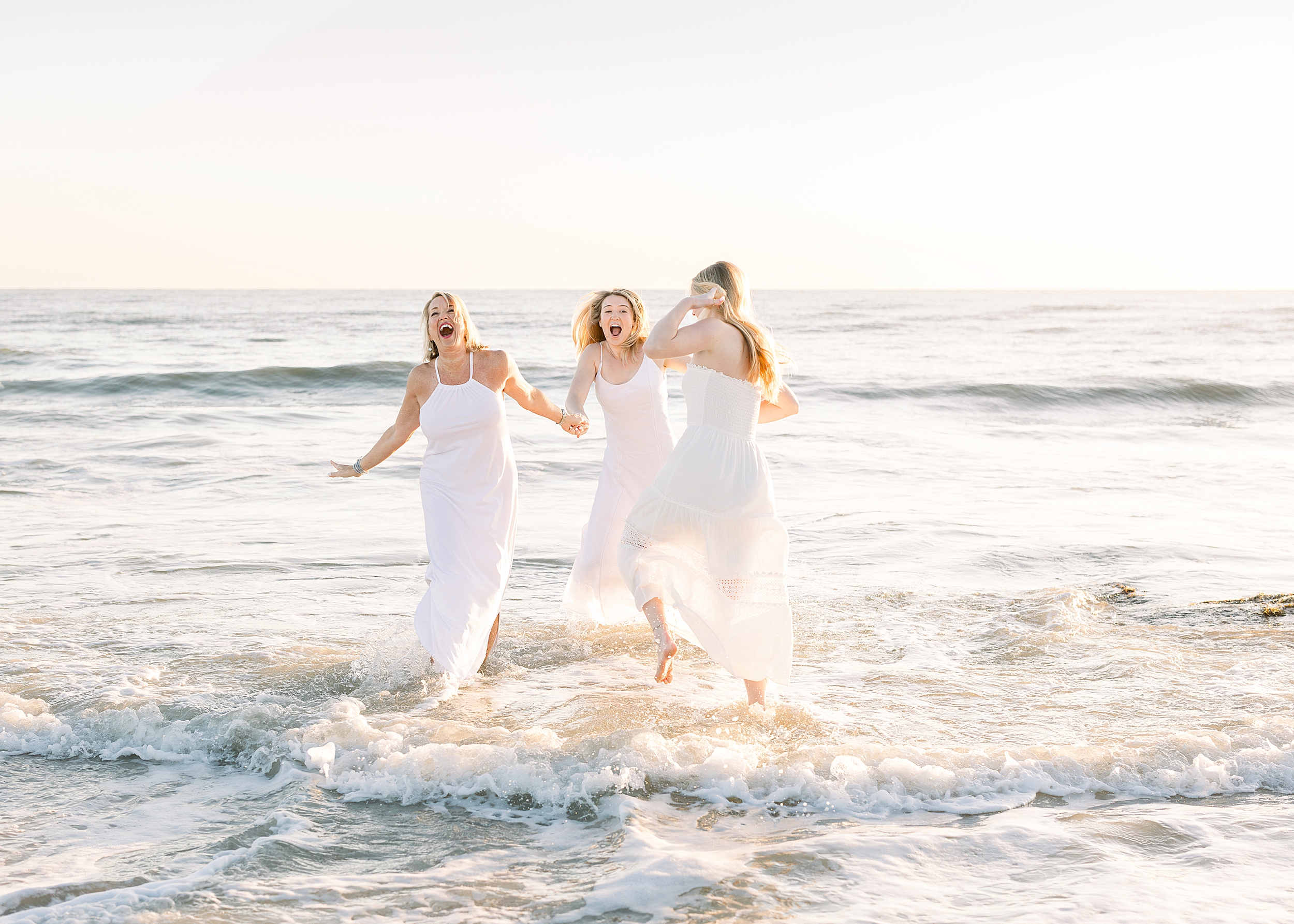 A light and airy sunrise family session portrait of an adult family playing in the water.