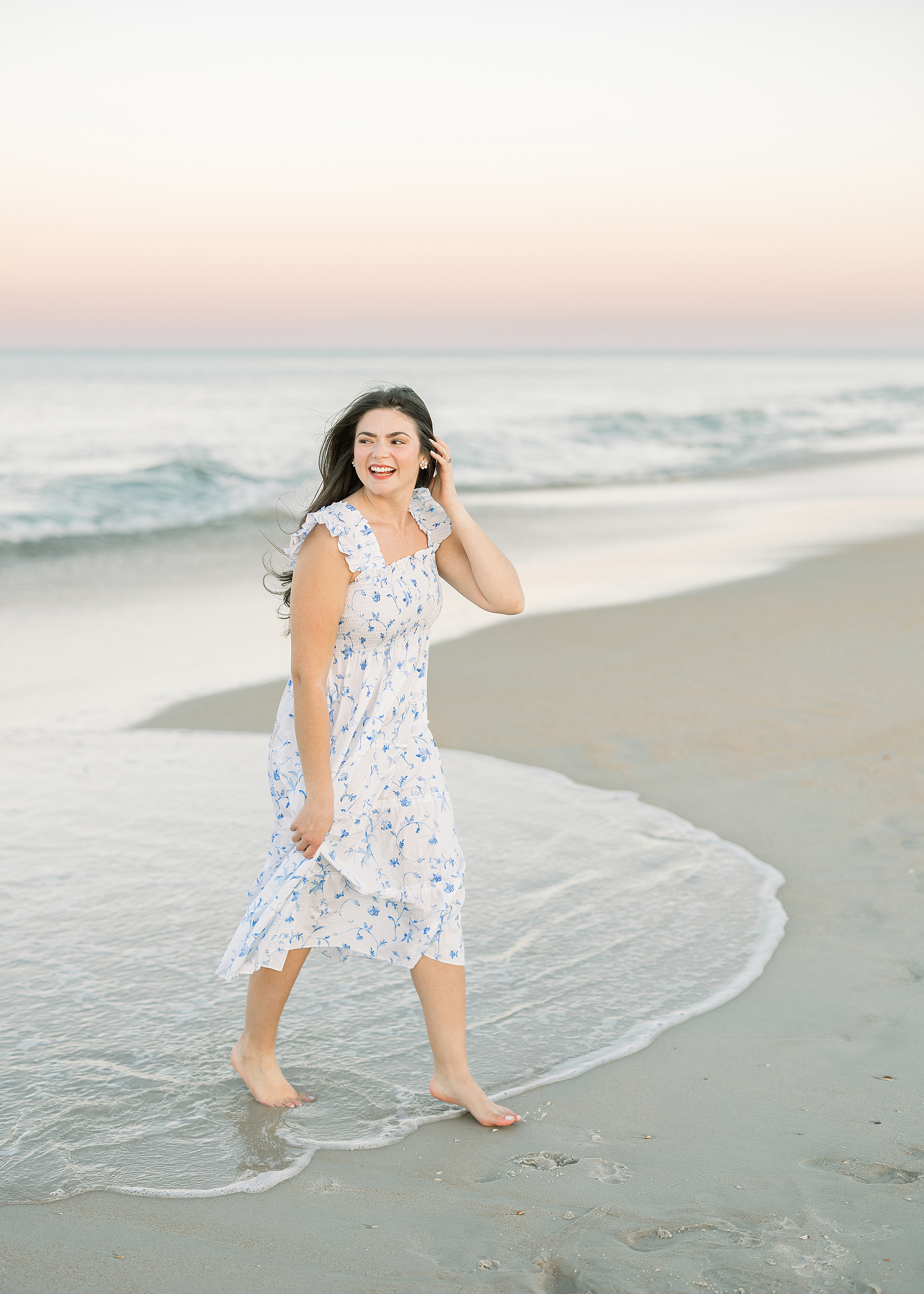 A pregnancy announcement portrait of a woman walking through the water on the beach at sunset.
