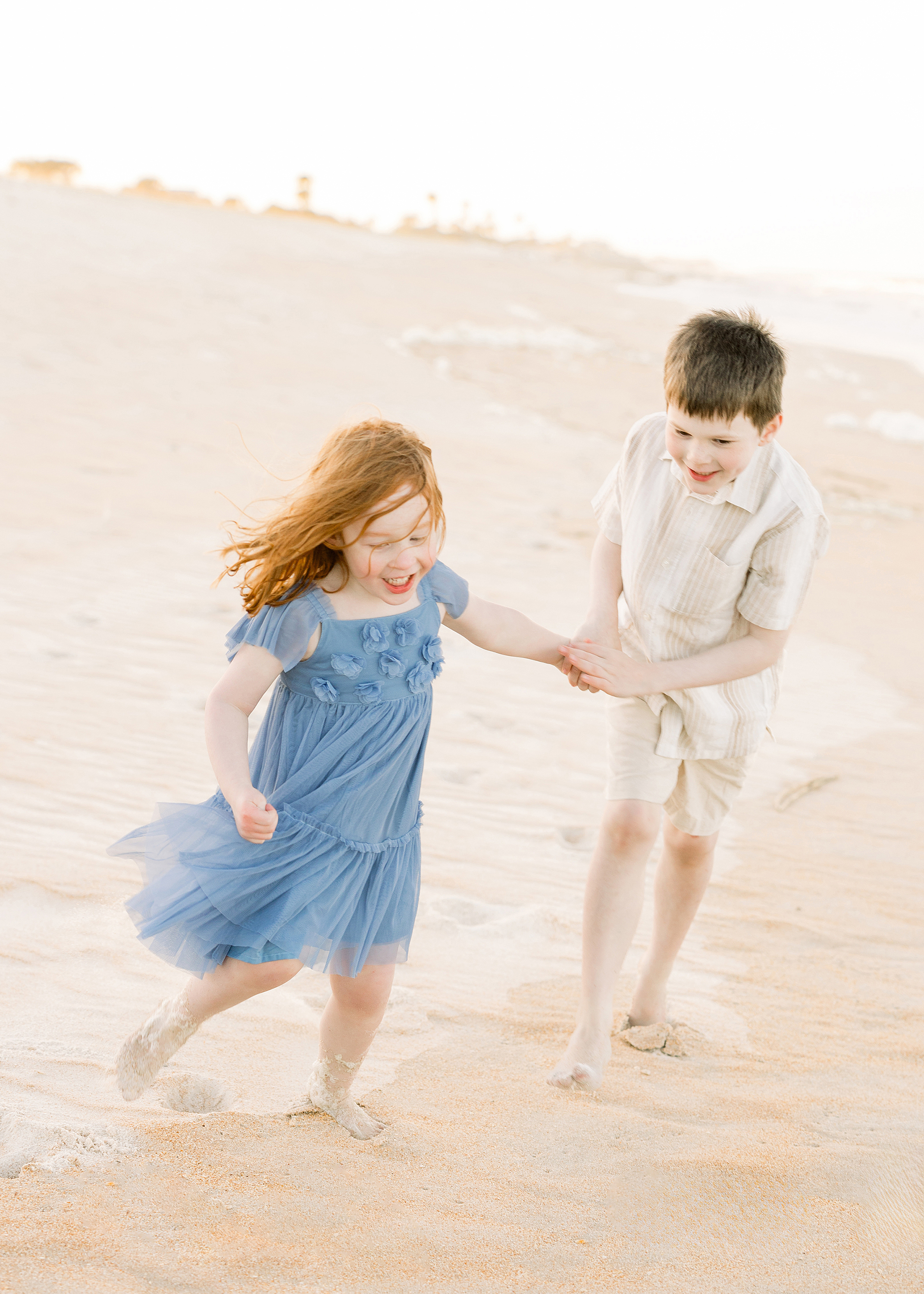 Two siblings play together on the sand at sunset.