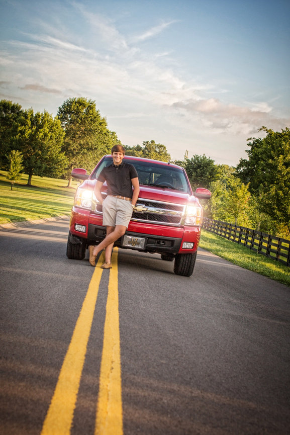 Person standing next to a red Chevrolet truck on a rural road surrounded by trees.