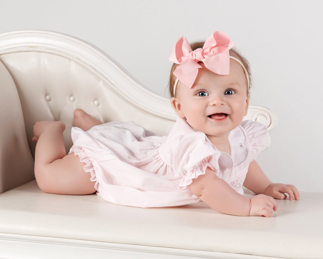Smiling baby girl with pink bow lying on a white couch